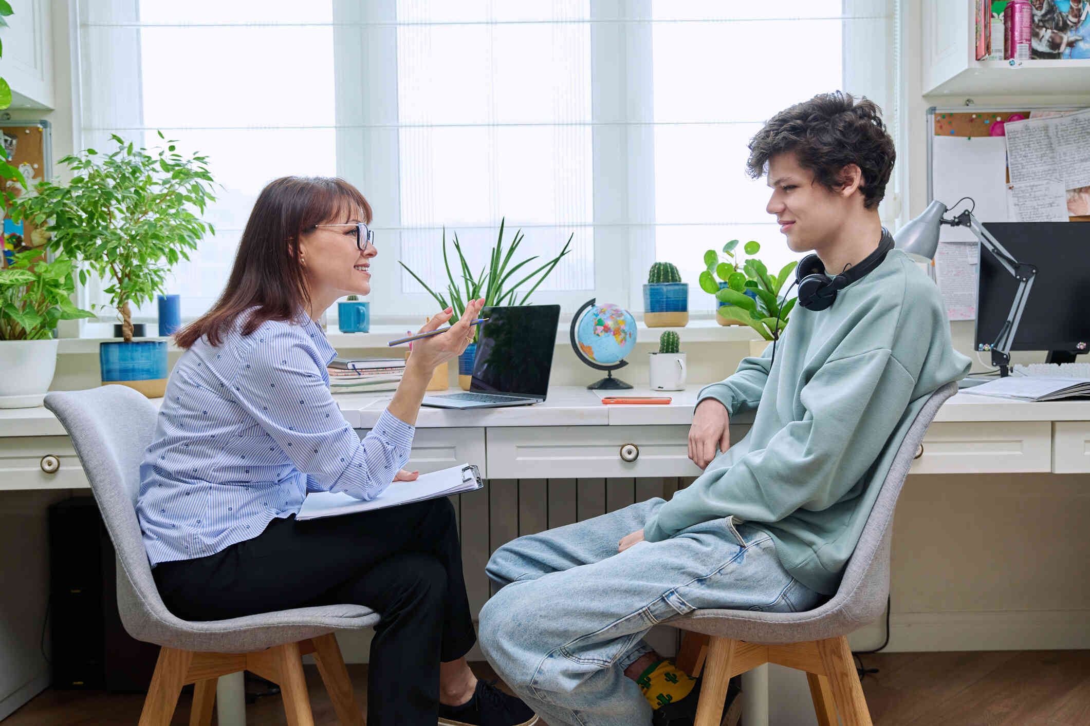 A teen boy sits in a chair across from his female therapist while listening to her talk.